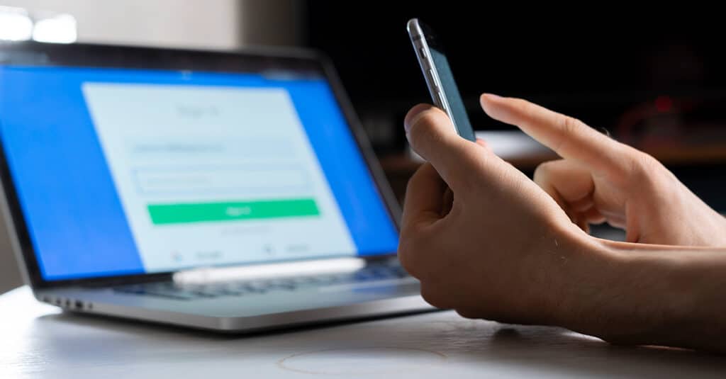 Person holding a phone and working using a laptop