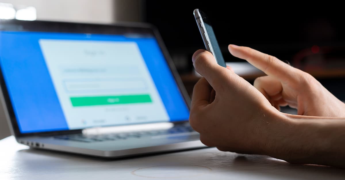 Person holding a phone and working using a laptop