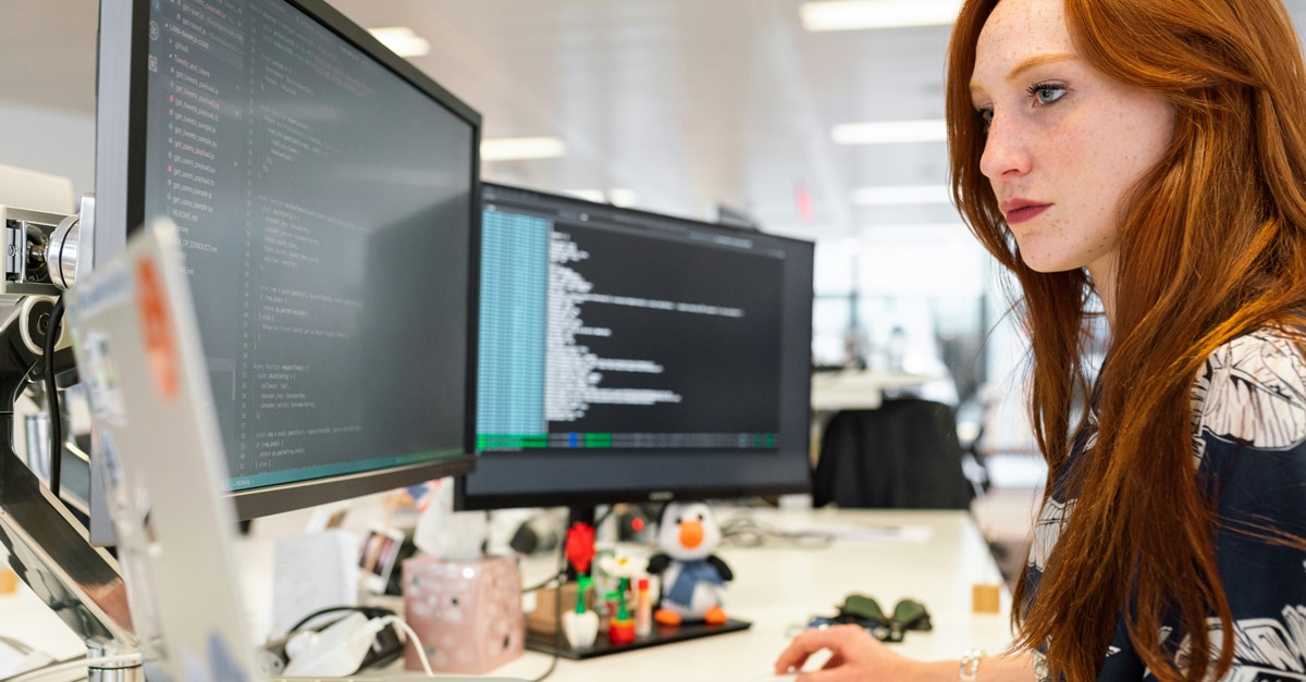 Red haired girl coding on two screens