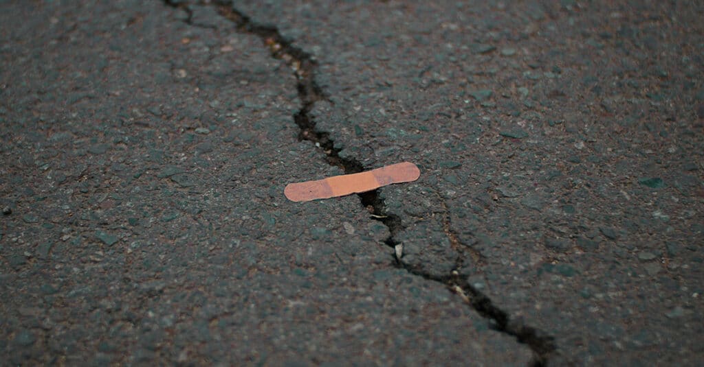 Large crack across concrete with small ineffective bandaid placed on it