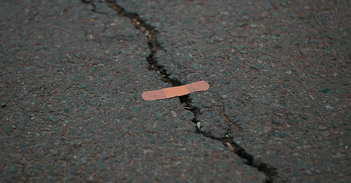 Large crack across concrete with small ineffective bandaid placed on it