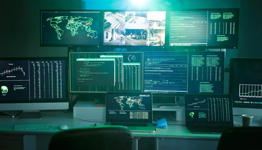 Security monitoring control room with multiple screens displaying surveillance feeds representing digital threat monitoring and cyber visibility